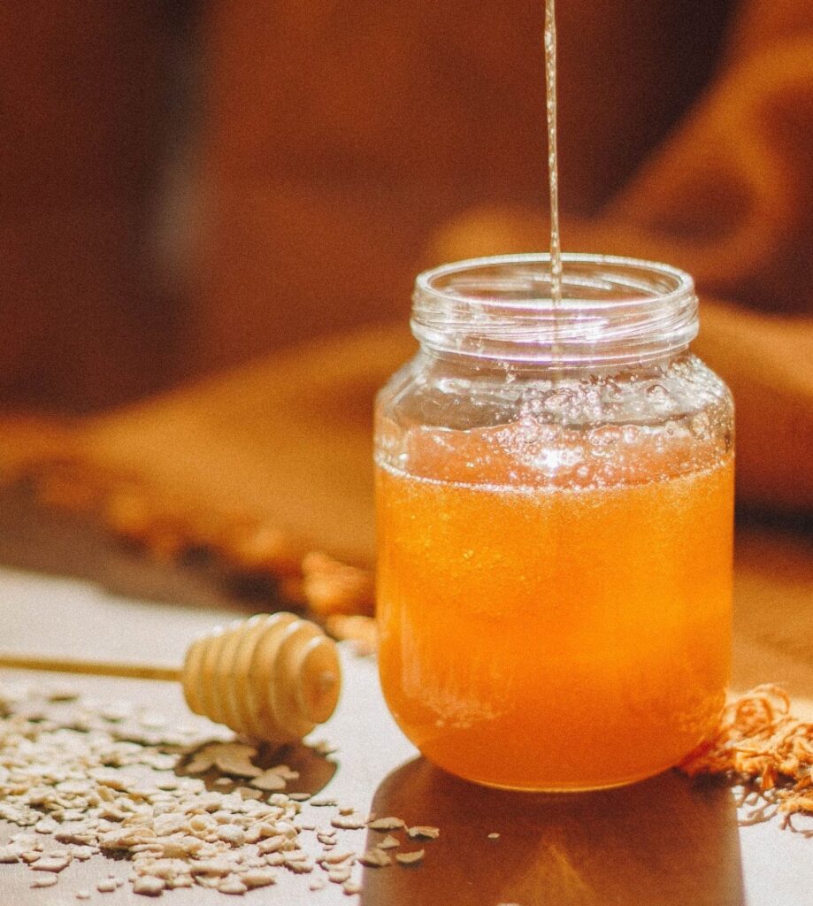 honey dripping into a honey jar next to a honey spoon